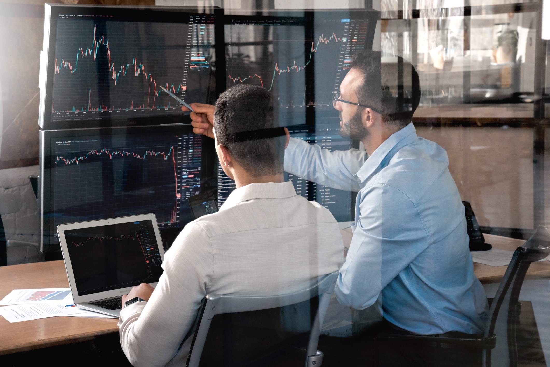Two successful trader sitting in office and looking at screen, checking cryptocurrency information data on finance market graph, pointing on monitor